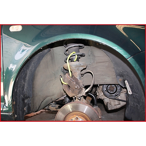 Nahaufnahme des Radkastens eines grünen Autos. Bremsscheibe, Federung, Stoßdämpfer und gelbe Leitungen sind zu sehen.